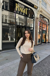 a lady wears a beige sweater with dark brown pants